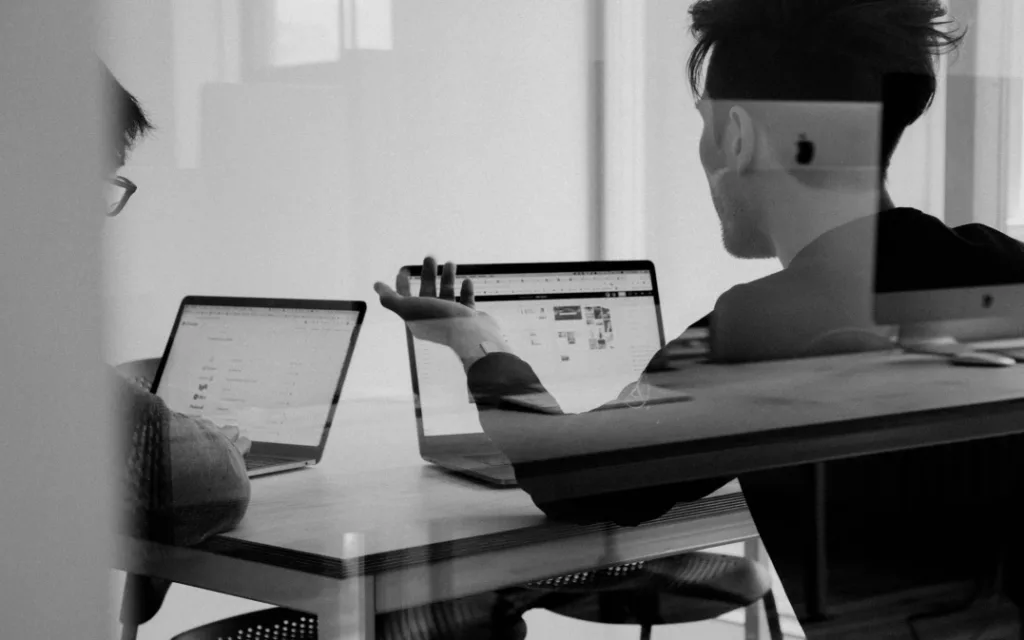 två personer i ett mötesrum med varsin laptop