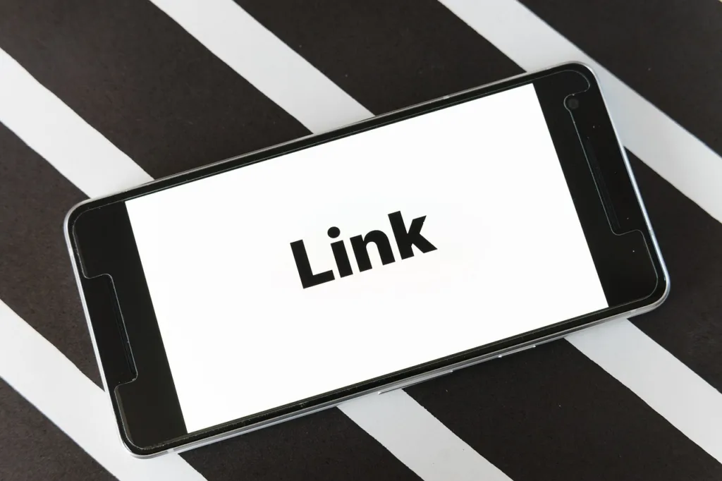 En mobiltelefon som ligger på ett svartvitrandigt underlag, med ordet 'Link' i stor svart text på skärmen.